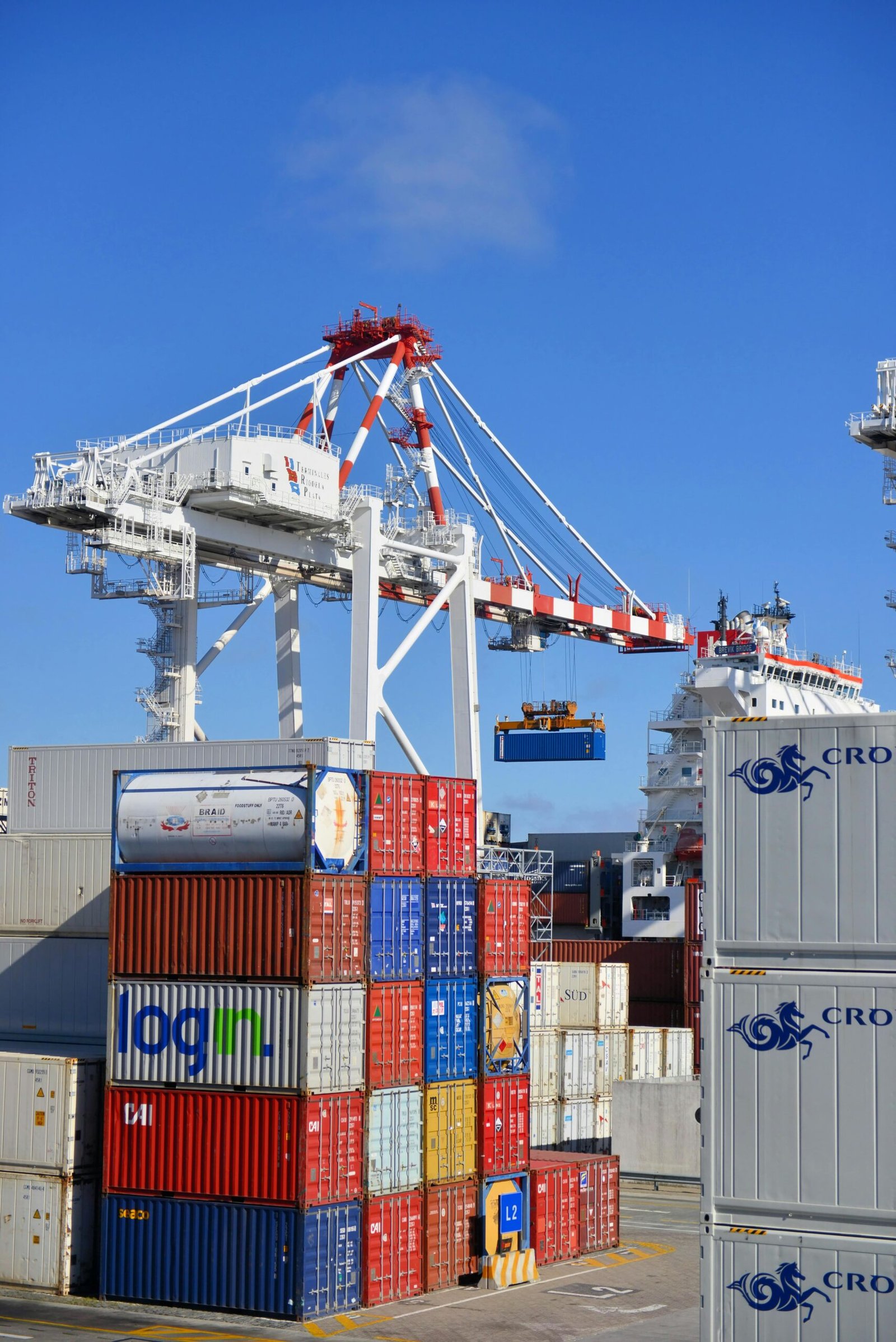 Colorful shipping containers stacked in a busy port with cranes overhead.