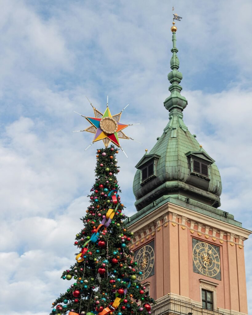 Warsaw Royal Castle tower with a decorated Christmas tree under a blue sky, capturing festive charm.