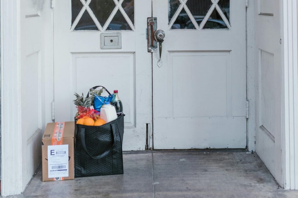 Front doorstep with grocery bag and parcel, representing contactless home delivery services.