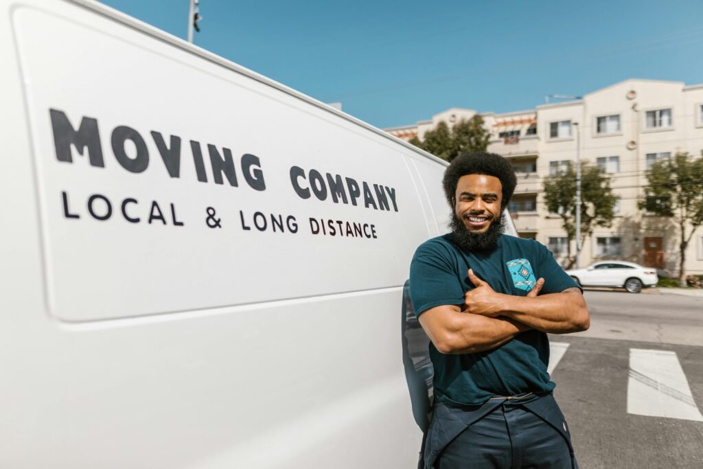 A cheerful mover standing confidently beside a moving company's van, ready for local or long distance relocation services.