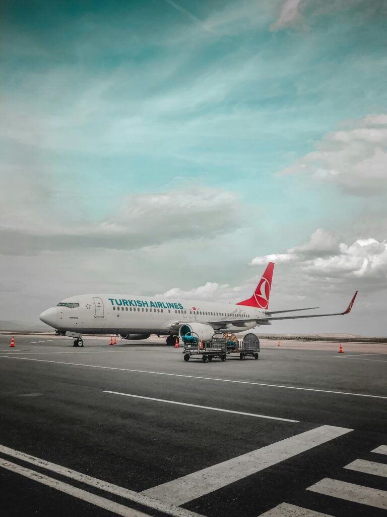 Turkish Airlines plane parked on airport tarmac with clear blue sky and clouds.