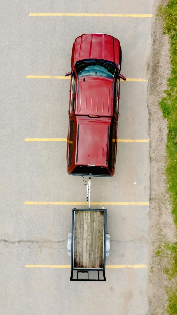 Aerial shot of a red car with a trailer parked on an empty lot with visible parking lines.